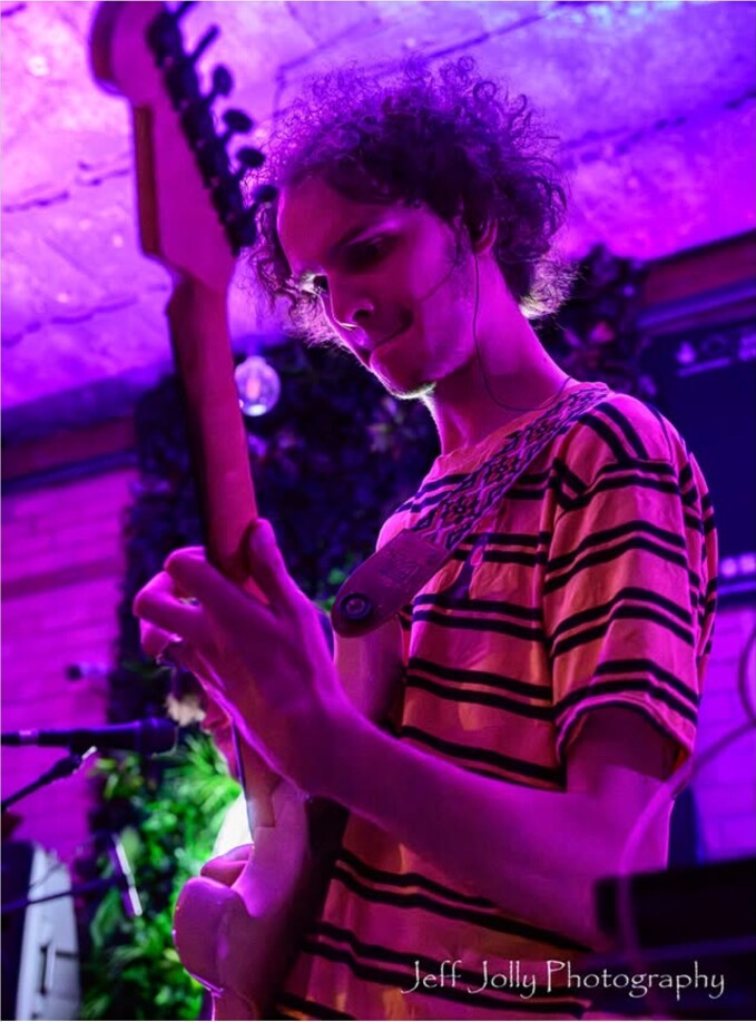 A guitarist playing under purple stage lights at Peggy McCools