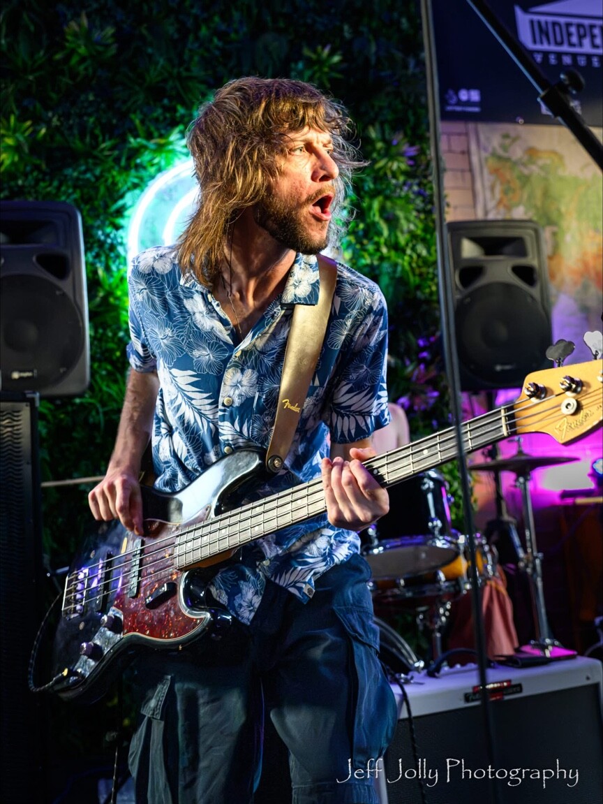 A bass guitarist performing in front of the Peggy McCools sign