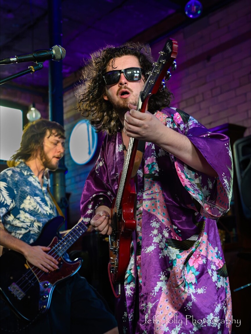 Two guitarists performing under purple lights at Peggy McCools