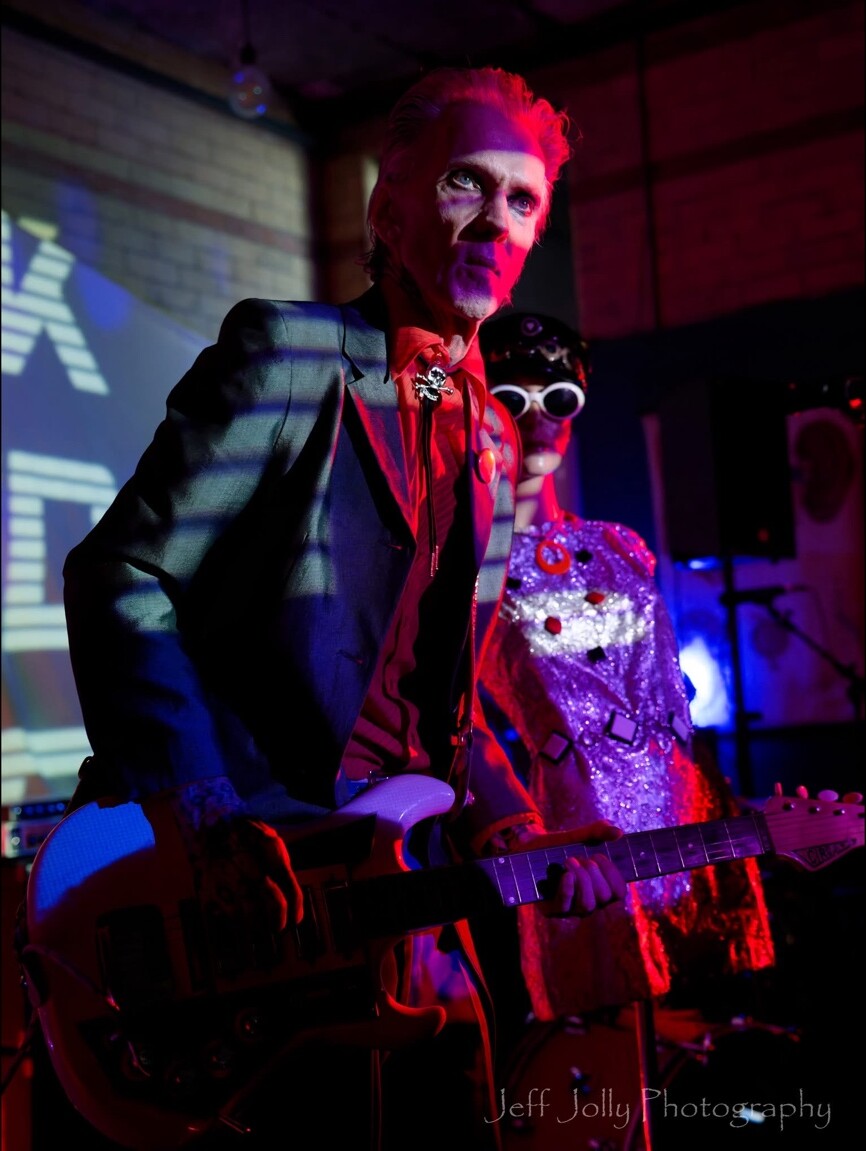 A guitarist performing beside a silver mannequin