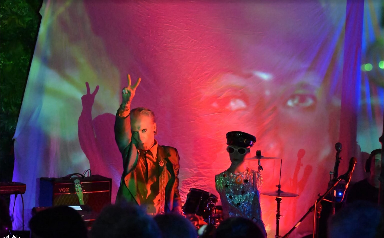 A theatrical band performing in front of projected faces