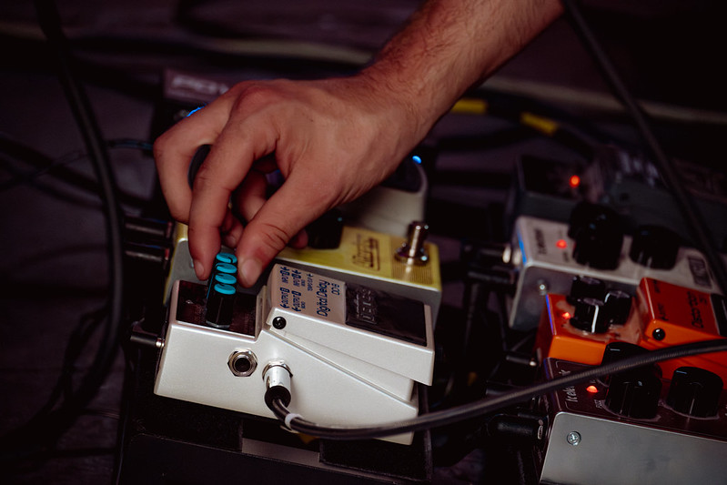 A musician adjusting a guitar effects pedal at Peggy McCools
